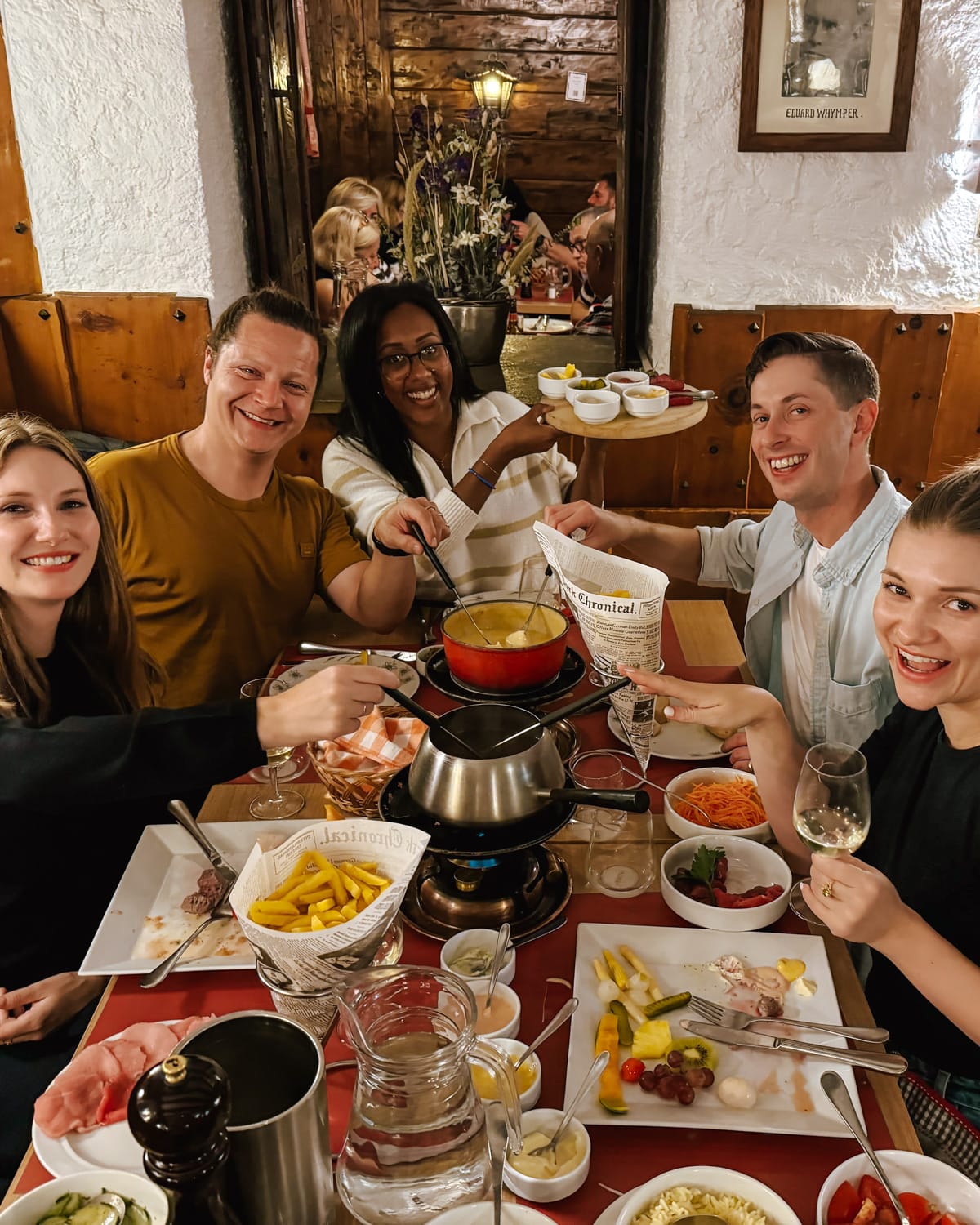 Friends eating cheese and meat fondue at Whymperstube