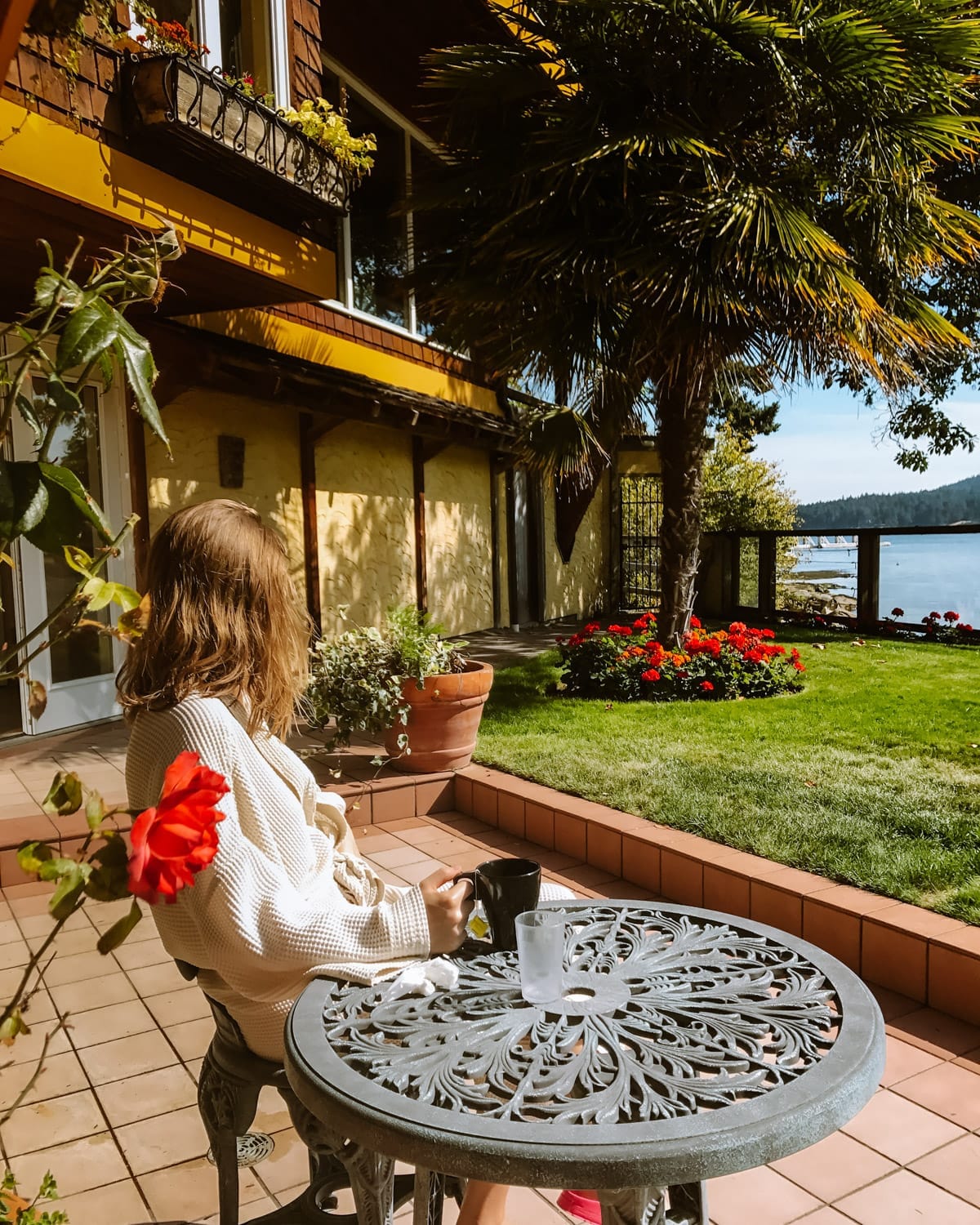 Cec sitting outside in a robe drinking tea with flowers and ocean views