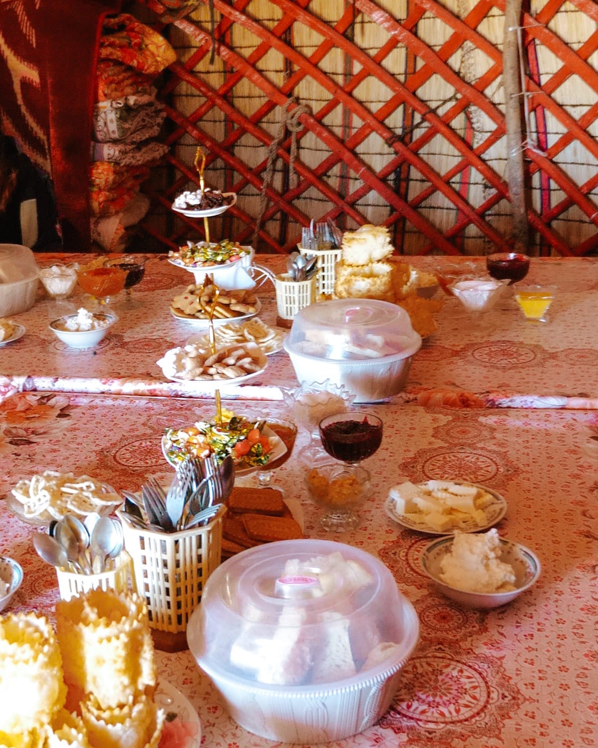 A table covered in a patterned cloth, set with an assortment of homemade breads, sweets, and bowls of dairy products inside a yurt.