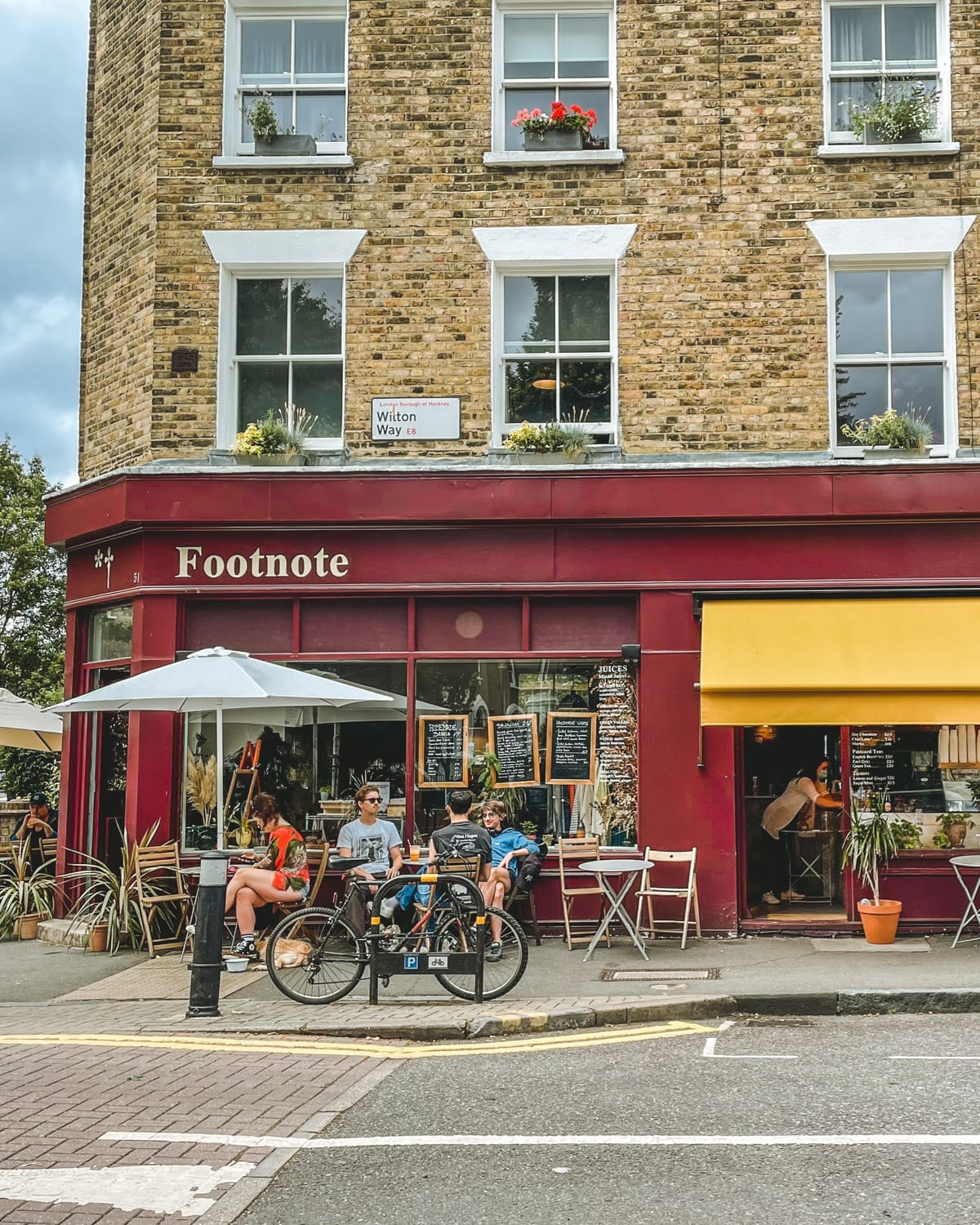 A street view of Wilton Way, with people dining outdoors and handwritten menu boards.