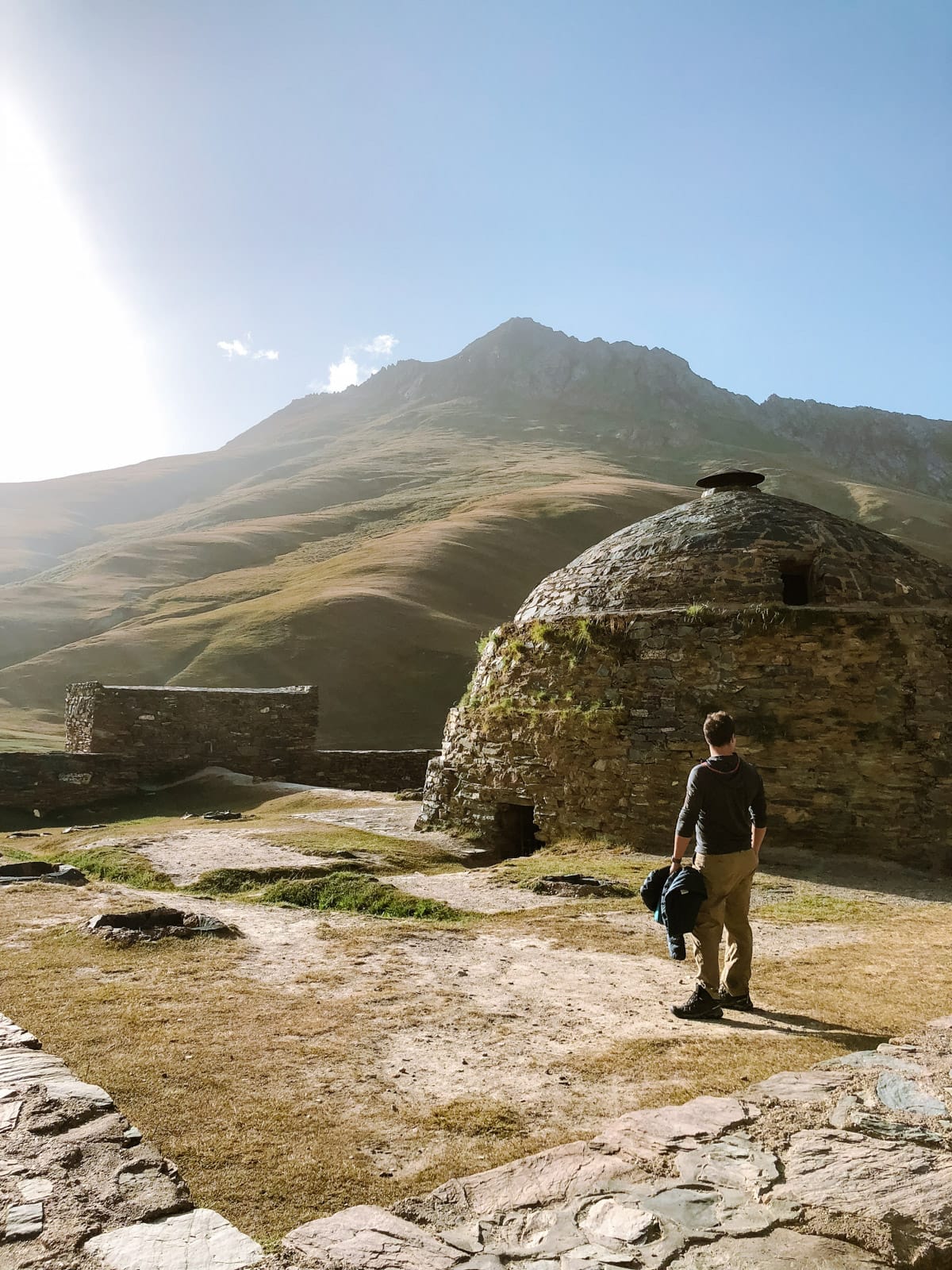 A traveler exploring the Tash Rabat Caravanserai with rolling hills and mountains in the background.