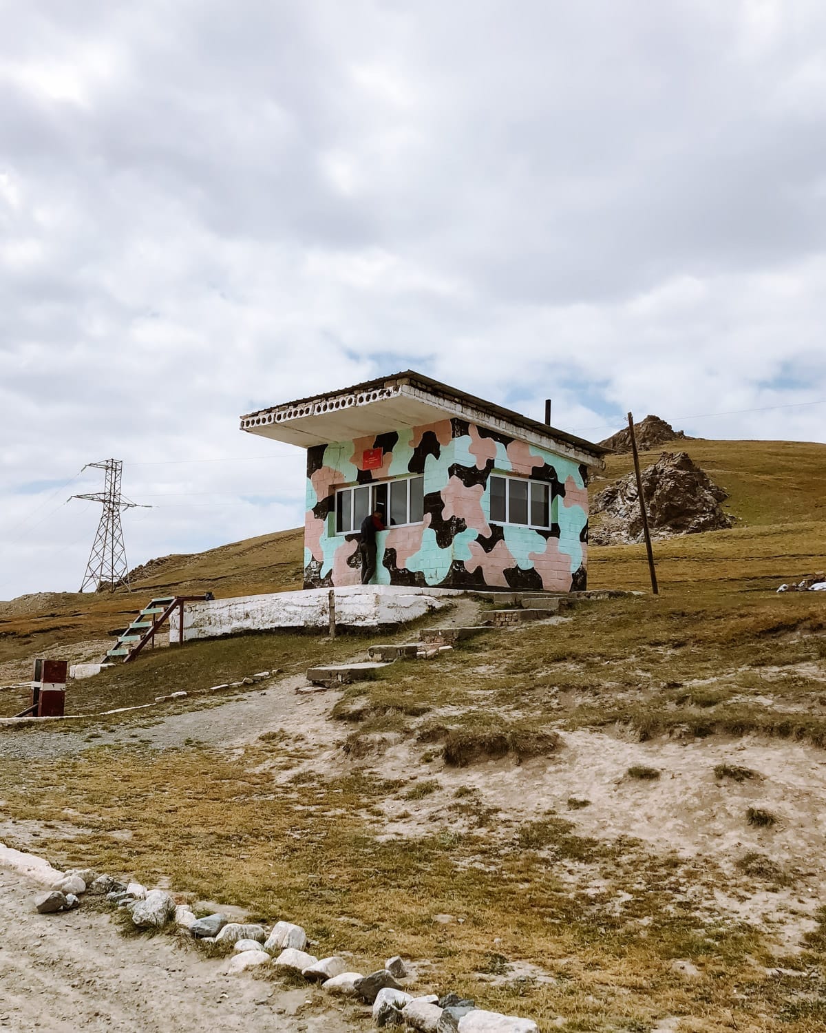 A colourful, camo-painted roadside checkpoint in the border zone between Kyrgyzstan and China, set against grassy hills.