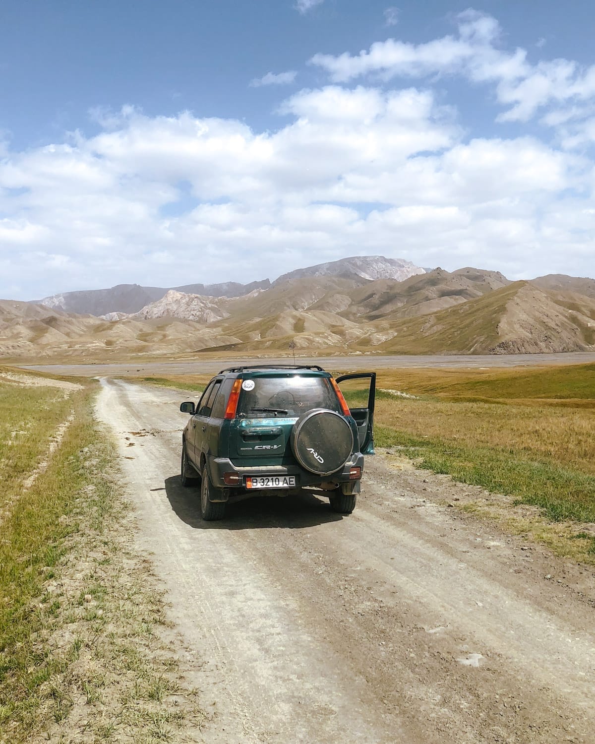 SUV parked on a dirt road in the Kel-Suu Region, surrounded by open grasslands and distant mountains.