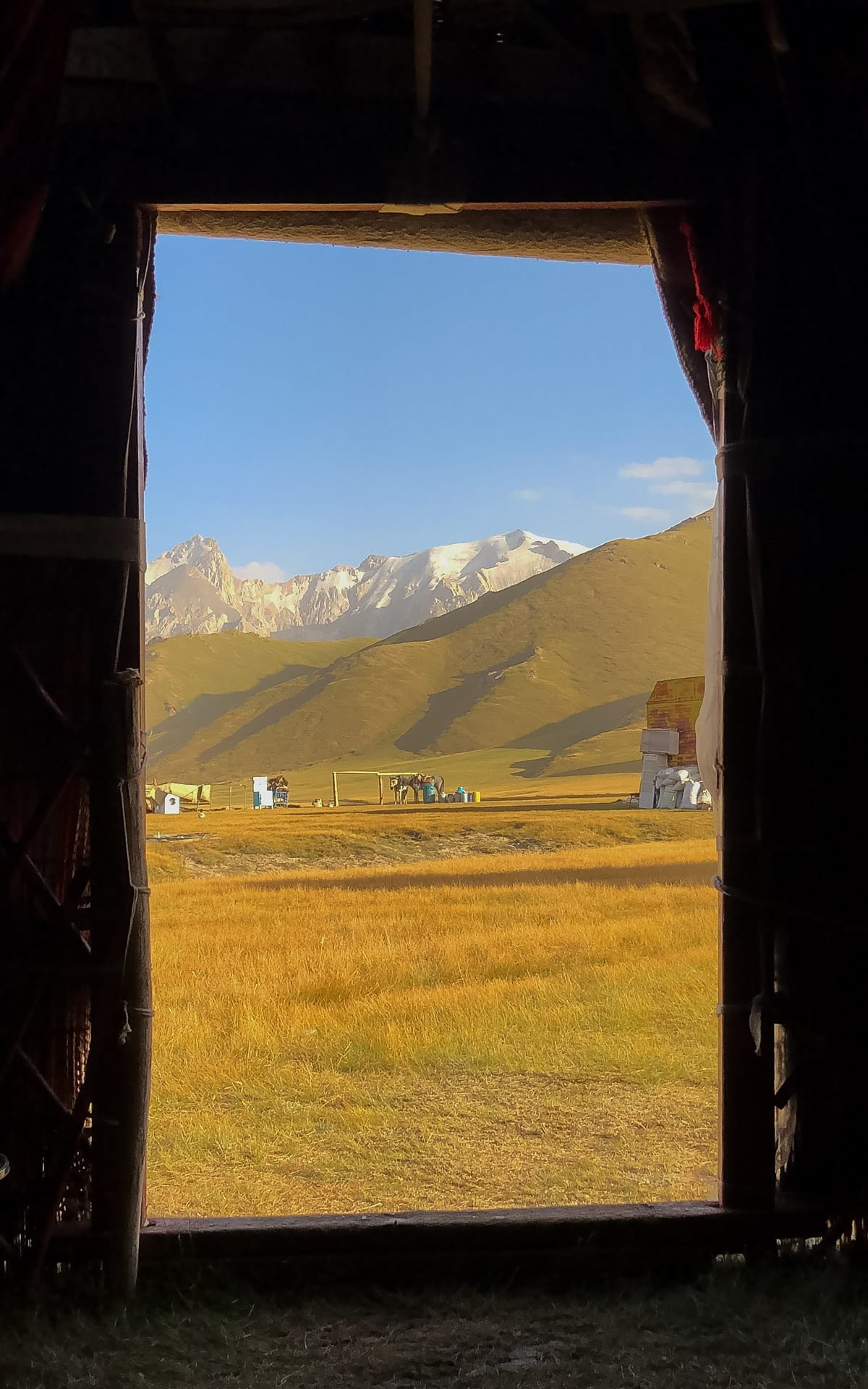 View of Kel-Suu's mountain landscape from inside a yurt, framing golden fields and distant peaks.