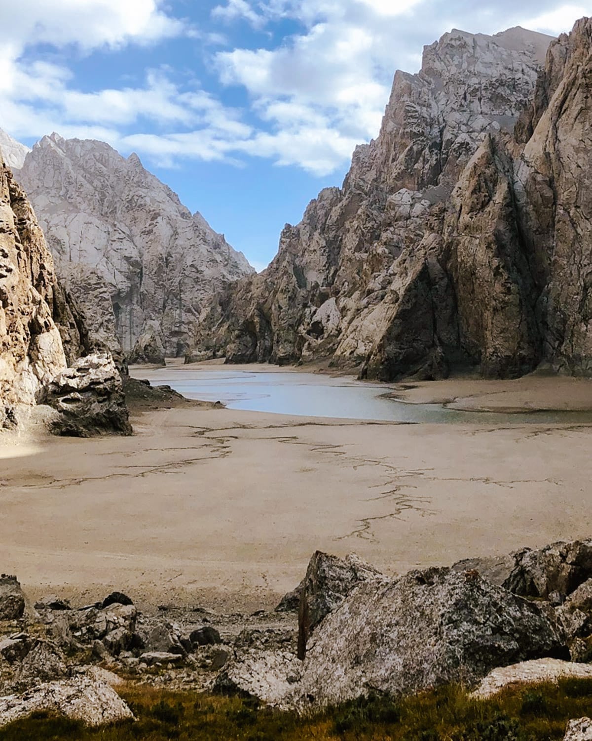 Towering cliffs surrounding a dry lake bed at Kel-Suu Lake, with clear skies above rugged rock formations.