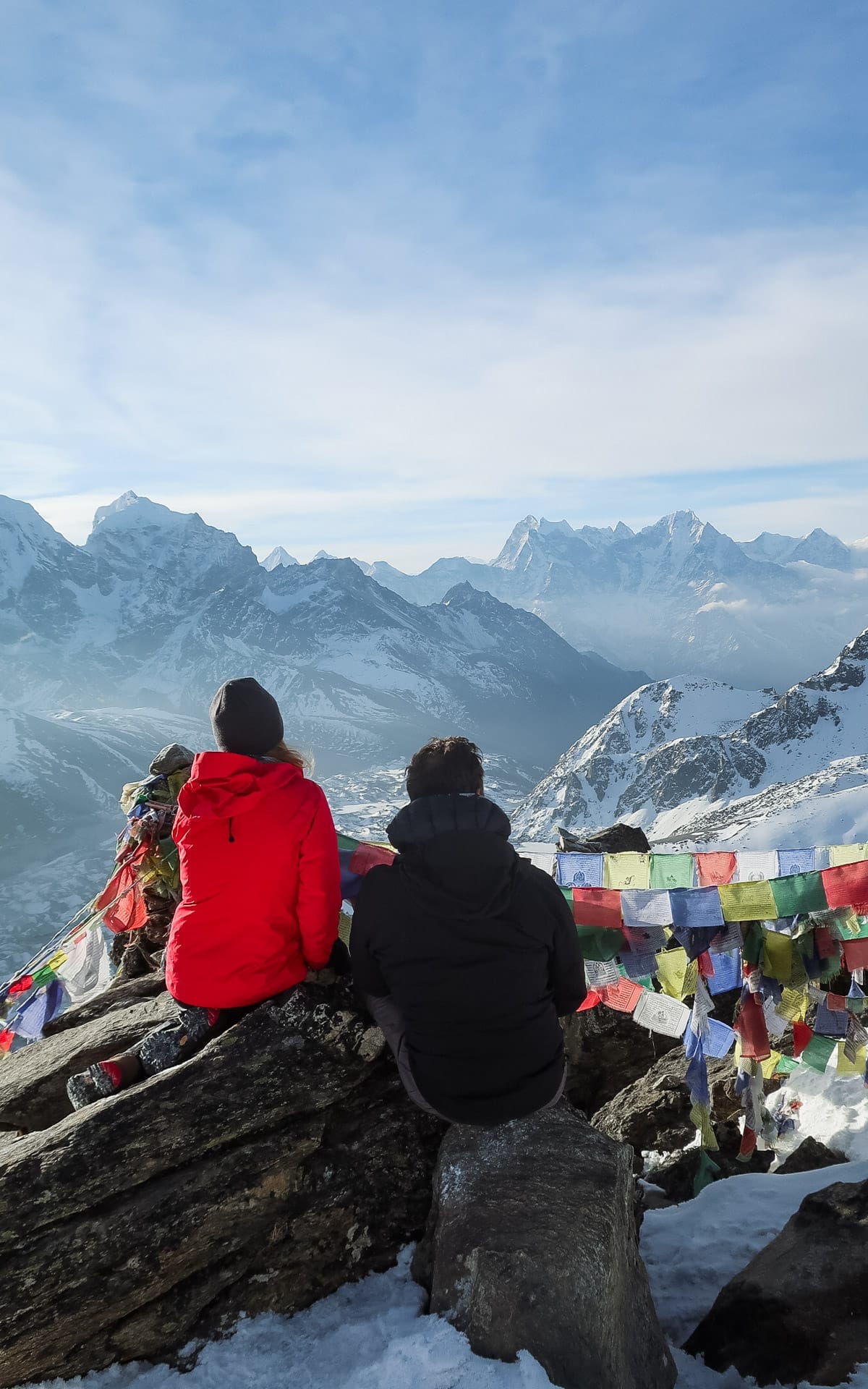  Cec and her partner Ari sitting on the snowy Gokyo Ri summit in Nepal overlooking some of the highest peaks in the world, with colourful prayer flags waving in the wind.