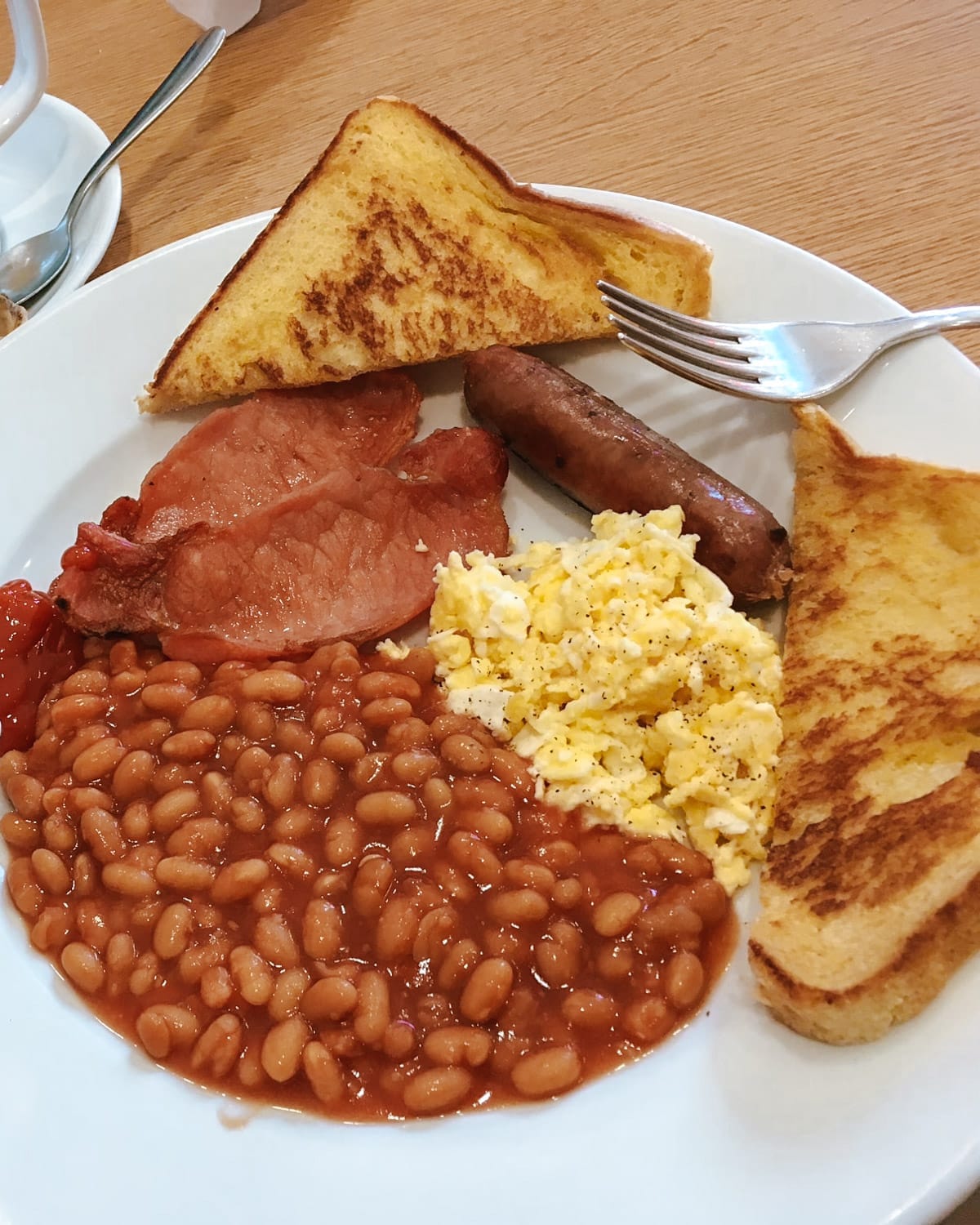 A classic British breakfast with baked beans, scrambled eggs, sausage, bacon, and toast.