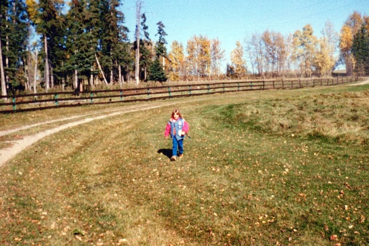 Cecily, 8 years old, walking on a grassy driveway at her childhood home in the countryside of Rocky Mountain House.