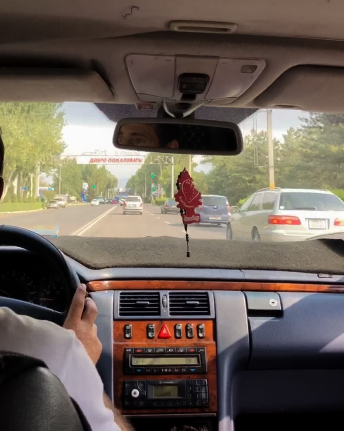 View from a car driving through Bishkek, Kyrgyzstan, with traffic and a road sign in Kyrgyz Cyrillic writing ahead.