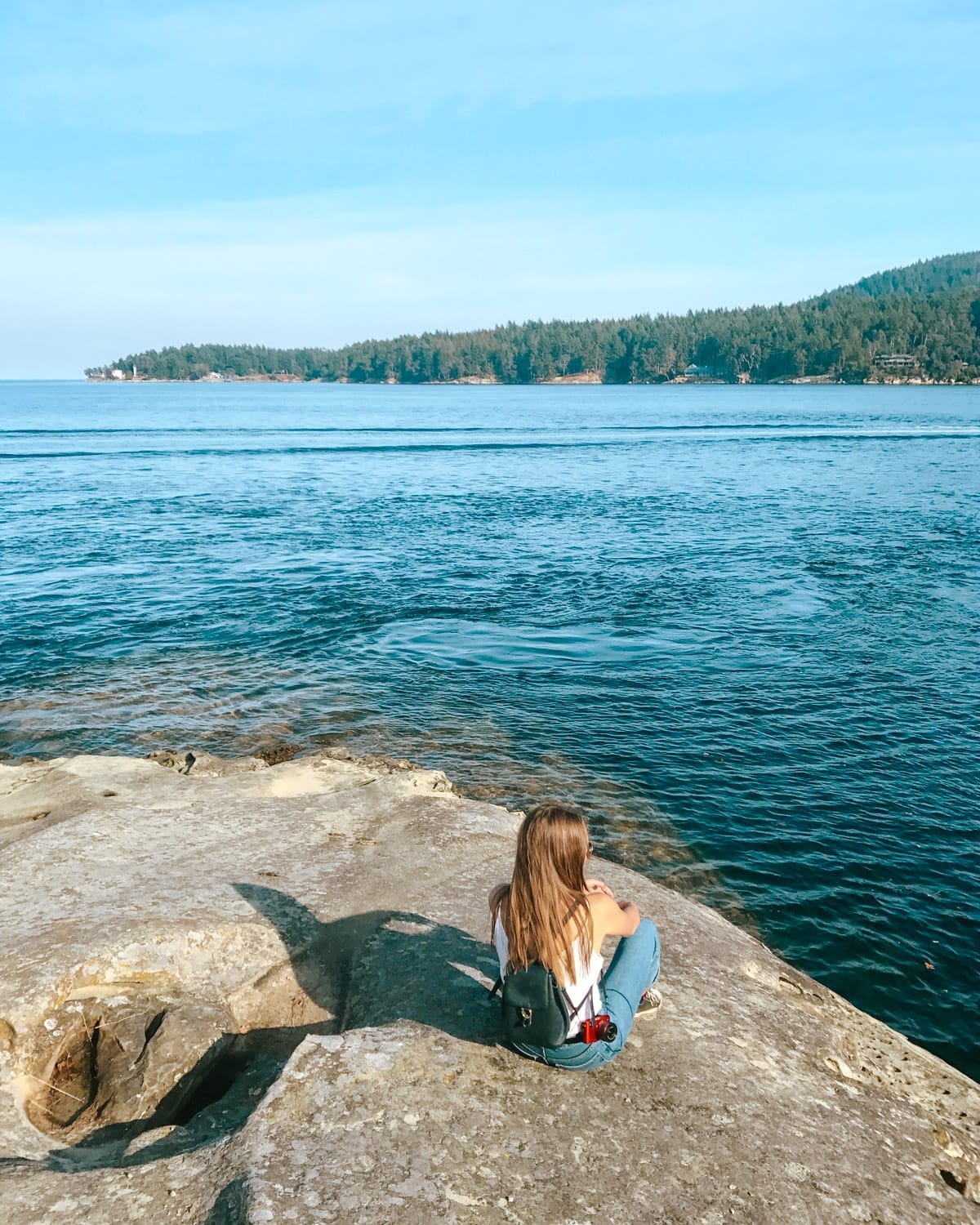 Cec's sister sitting on a bluff overlooking the ocean and forested coastline.