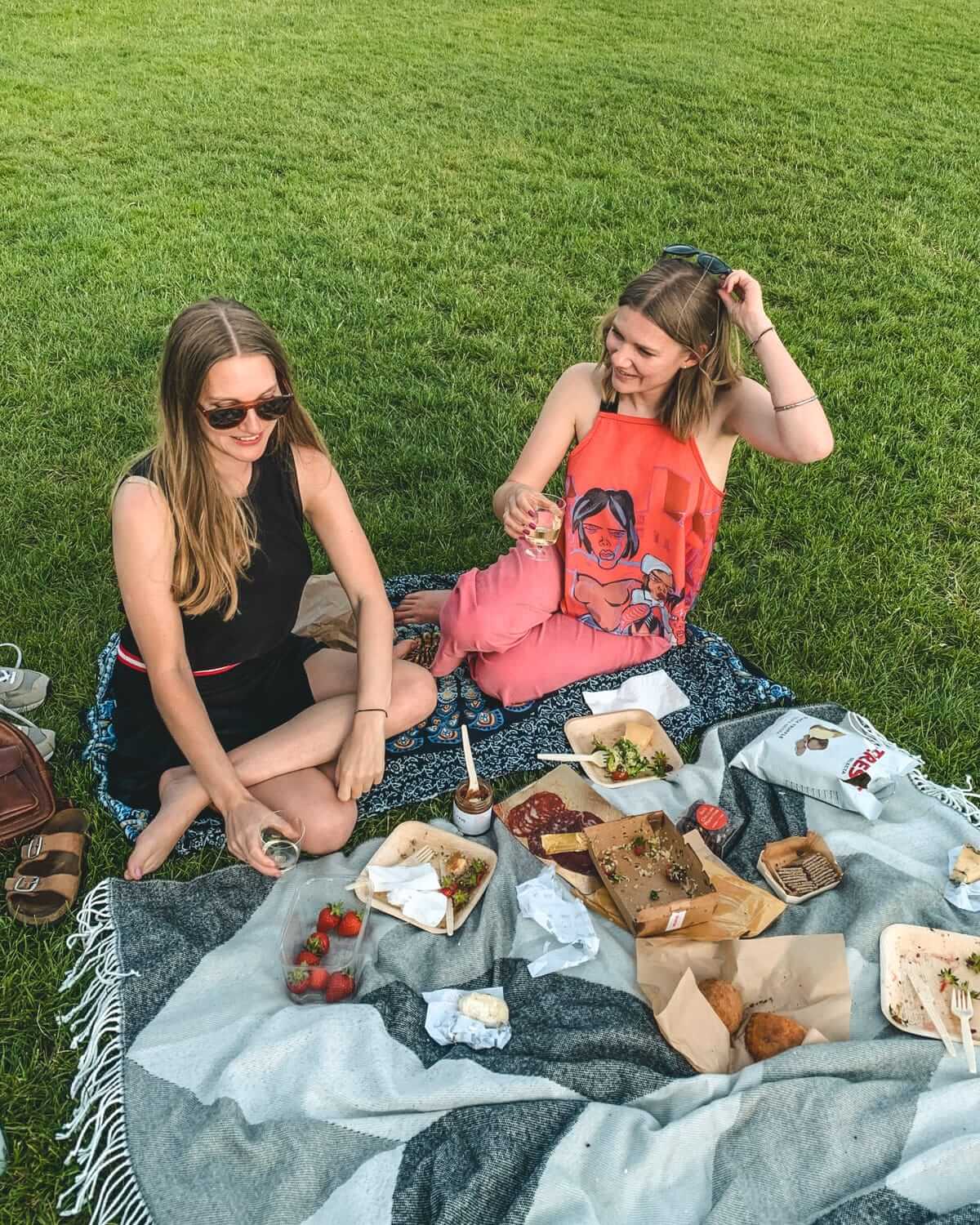 A blanket with picnic food and wine, set in the grass on Primose Hill.