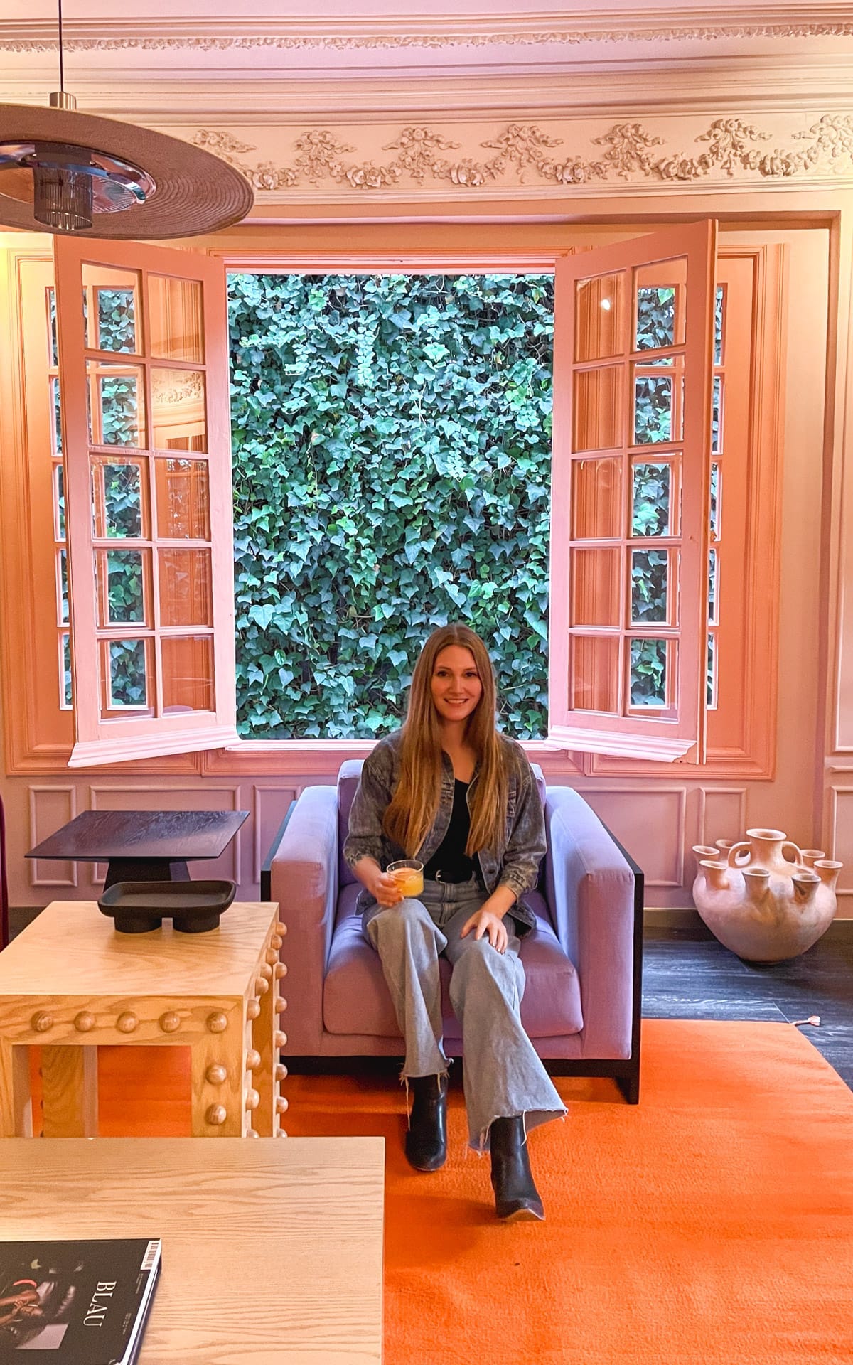 Cec sitting in a denim jacket at a design-forward boutique hotel in Mexico City with pre-Hispanic influenced furniture.