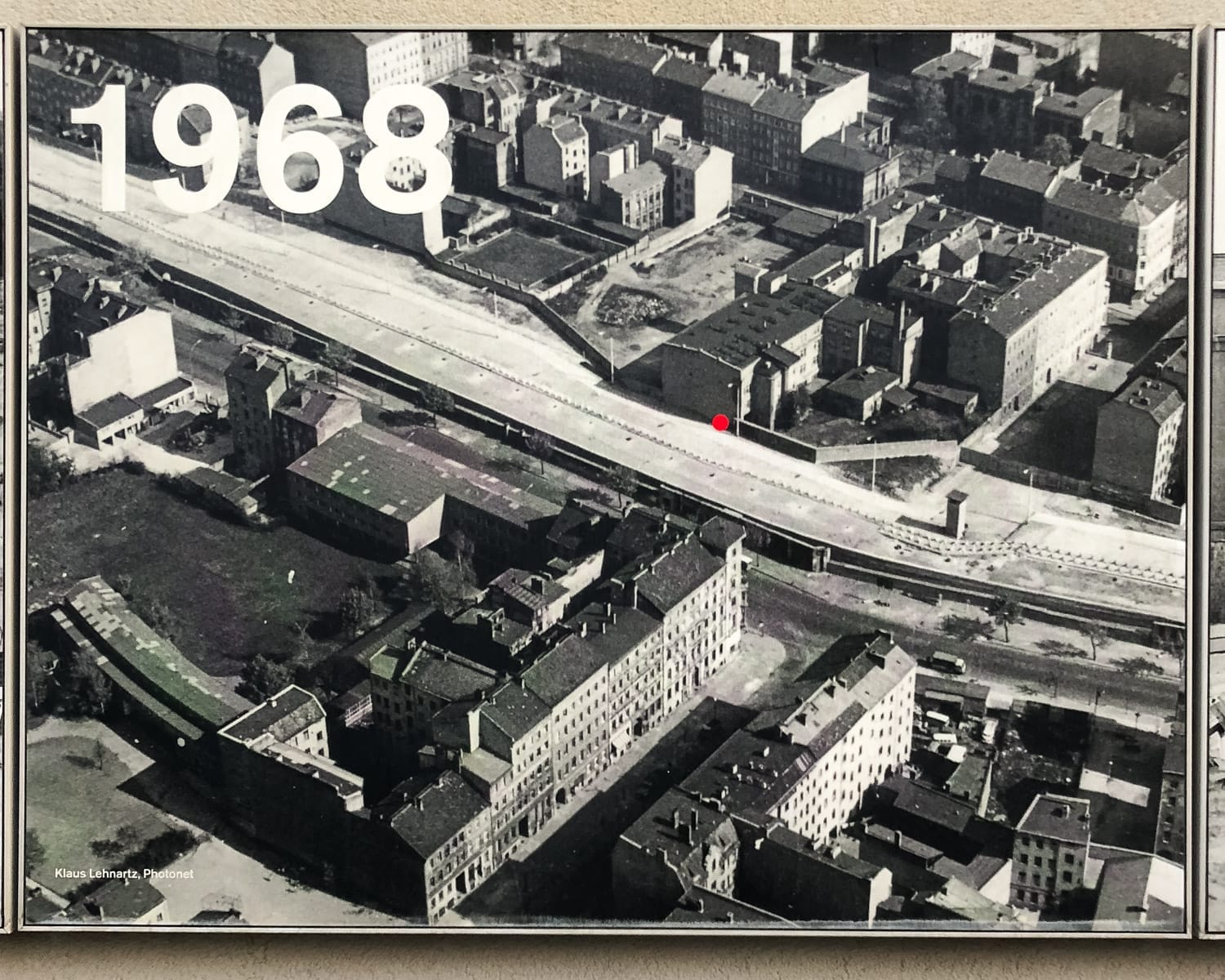 A black-and-white aerial photo from 1968 showing the Berlin Wall dividing streets and buildings, with a red dot marking a spot.