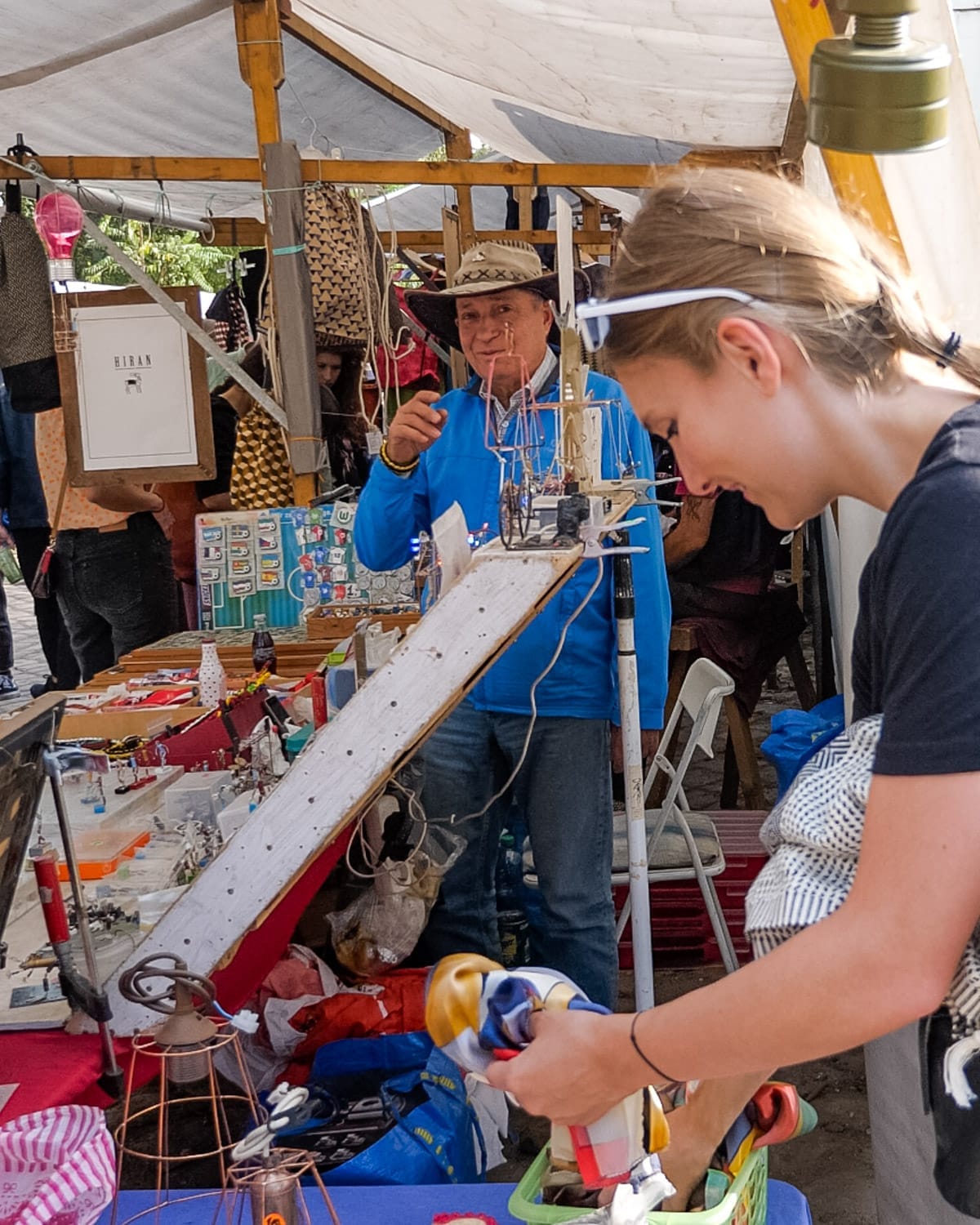 Cec browsing a Mauerpark Market stall, while a vendor in a hat smiles behind a table of handmade crafts and trinkets.